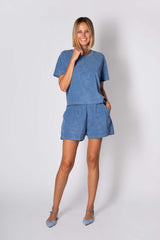 Donna sorridente in completo estivo blu in cotone, composto da t-shirt e pantaloni corti, elegante e comodo per le giornate calde.