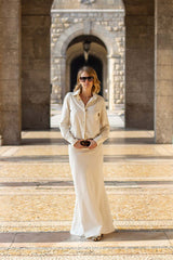 Woman wearing a stylish white outfit with sunglasses, walking elegantly in an architectural setting.
