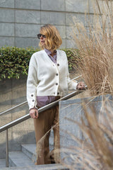 Woman wearing a stylish white cashmere cardigan with buttons, standing by a stair railing in an urban setting.