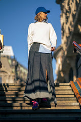 Woman in casual outfit with a white sweater and long skirt, wearing a blue cap, walking down outdoor stairs.