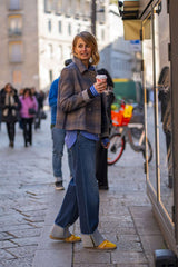 Woman in a stylish outfit with a plaid jacket and yellow shoes holding a coffee cup on a city street.