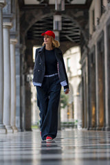 Woman in red cap and stylish outfit walking through an elegant corridor with a checkered floor.