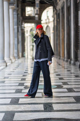 Woman in a black double-breasted peacoat and red cap, posing stylishly in an elegant stone corridor.