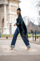 Model wearing a chic velvet kimono with jeans and heels, walking confidently in an urban park setting.