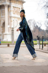 Model walking in a stylish kimono velvet coat paired with jeans and heels, showcasing elegance outdoors.