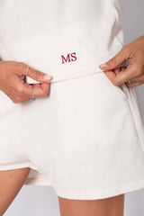 Close-up of a woman showing personalized shorts with MS embroidery in red on soft cotton fabric.