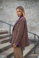 Woman wearing a stylish over-sized double-breasted blazer with a check pattern and purple details, standing on steps.