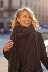 Smiling woman in a stylish striped scarf, showcasing casual winter fashion outdoors.