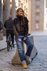 Woman wearing a stylish cashmere crew neck sweater with a scarf, sitting on a street in casual jeans.