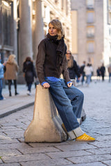 Woman in a stylish outfit sitting on a street corner, showcasing urban fashion and casual chic vibes.