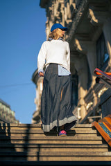 Woman wearing a stylish pleated denim skirt with a white sweater and cap, walking down outdoor stairs.