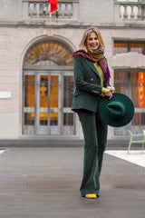 Woman in a stylish green velvet double-breasted suit with a colorful scarf and hat, posing outdoors.