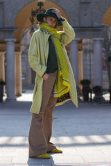 Model showcasing a cashmere jacquard scarf, dressed in stylish coat, hat, and wide-leg pants outdoors.
