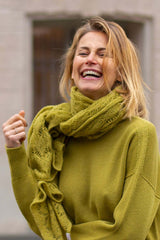 Woman smiling brightly wearing a green sweater and a matching scarf, showcasing comfort and style.