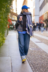 Woman in a blue cap and scarf walking on a city street with coffee cup, wearing stylish casual outfit.