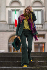 Fashionable woman in a colorful scarf, green outfit, walking down steps with a stylish hat.