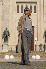 Model in stylish wide-legged wool pants and a long coat, showcasing modern elegance against an architectural backdrop.