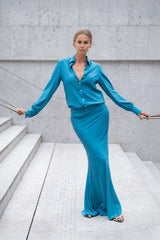 Woman in a turquoise satin outfit posed elegantly on outdoor steps.