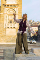 Woman wearing loose-fit printed shirt with ruffles and oversized pants, standing in an urban environment with historical architecture.