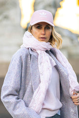 Woman wearing a pink cashmere lace scarf with a stylish grey coat and a pink cap, showcasing a modern, chic look.