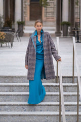 Model showcasing a stylish herringbone coat over a blue dress while walking down outdoor stairs.