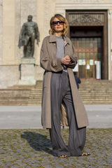 Fashionable woman wearing a trench coat with sunglasses, standing in an urban setting.