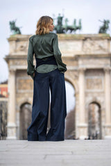 Woman in a sophisticated green blouse and wide-leg pants, posing in front of a grand arch monument.