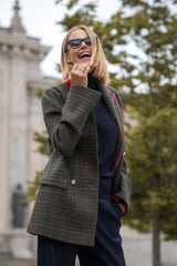 Stylish woman wearing a plaid double-breasted blazer with sunglasses, smiling outdoors.