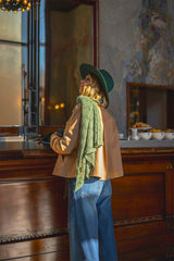 Woman wearing a cashmere lace scarf and green hat, styled with a chic jacket in a cozy café setting.