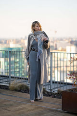 Elegant woman in grey cashmere outfit with a scarf, standing on a rooftop with city view.