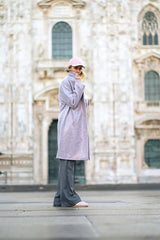 Model wearing a stylish sparkly boucle coat and cap, posing in front of a historical building.