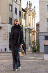 Elegant woman in blue velvet suit walking in city square with historic buildings in the background.