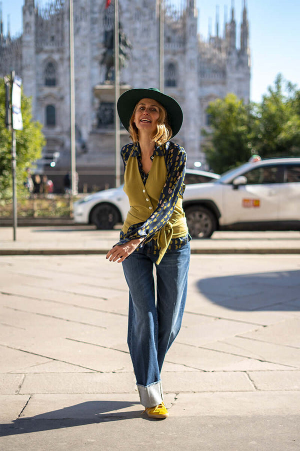 Stylish woman in a green vest and patterned shirt, smiling outdoors in Milan, showcasing a casual chic look.