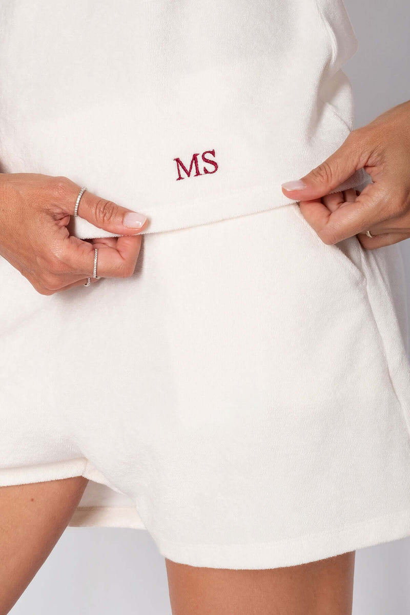 Close-up of a woman showing personalized shorts with MS embroidery in red on soft cotton fabric.