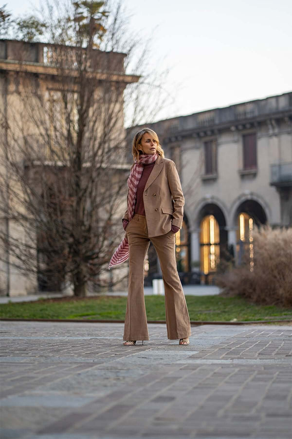 Woman wearing a camel velvet double-breasted suit with flared pants and a scarf, posing outdoors.