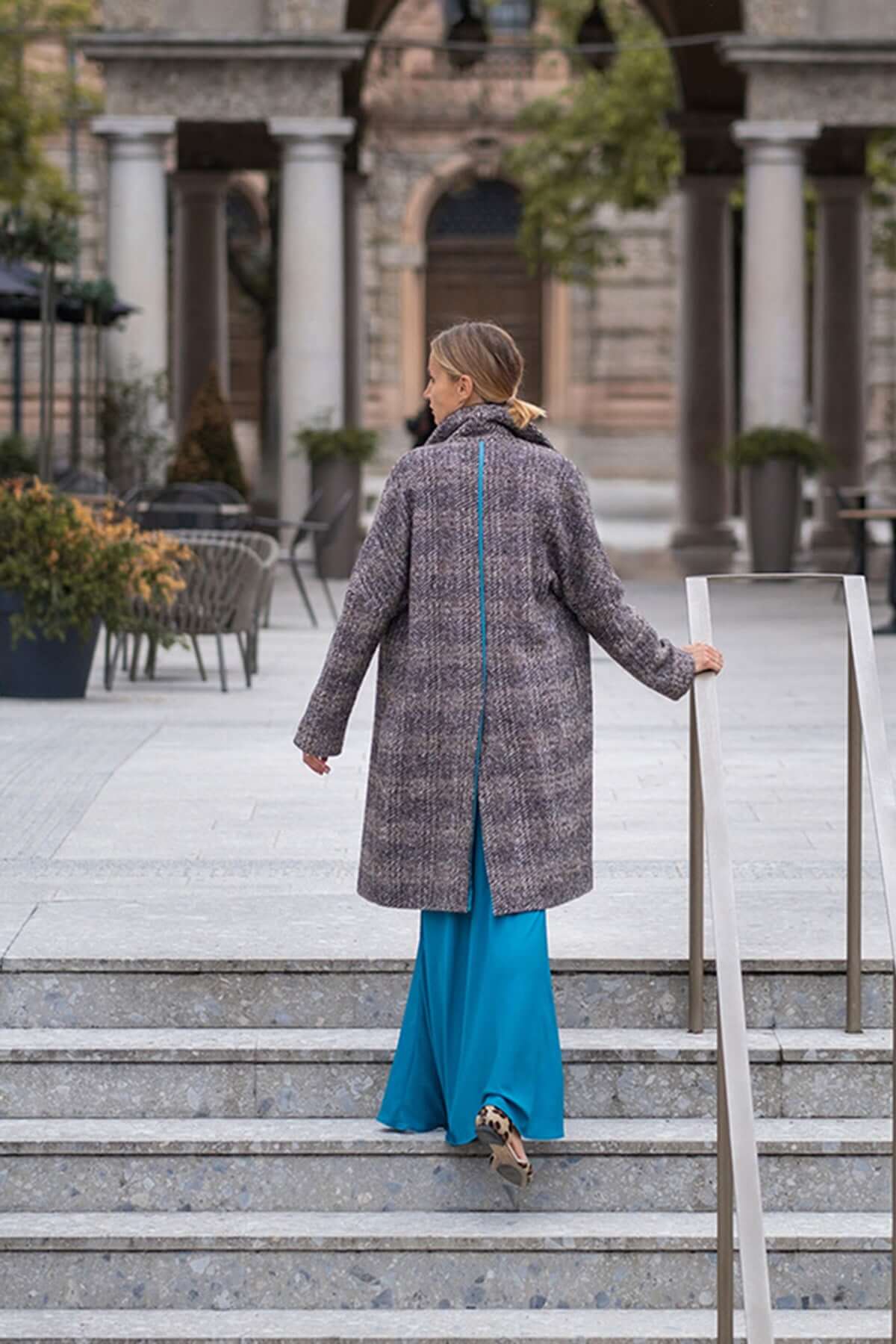 Woman wearing a stylish houndstooth coat over a blue dress, walking down outdoor steps.