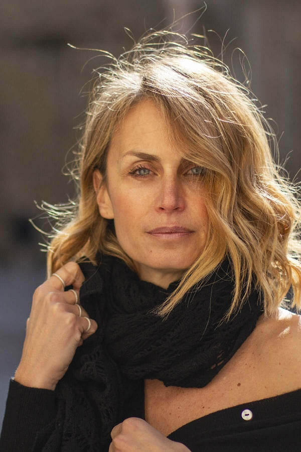 Woman wearing a black cashmere lace scarf, showcasing elegance and sophistication in natural sunlight.