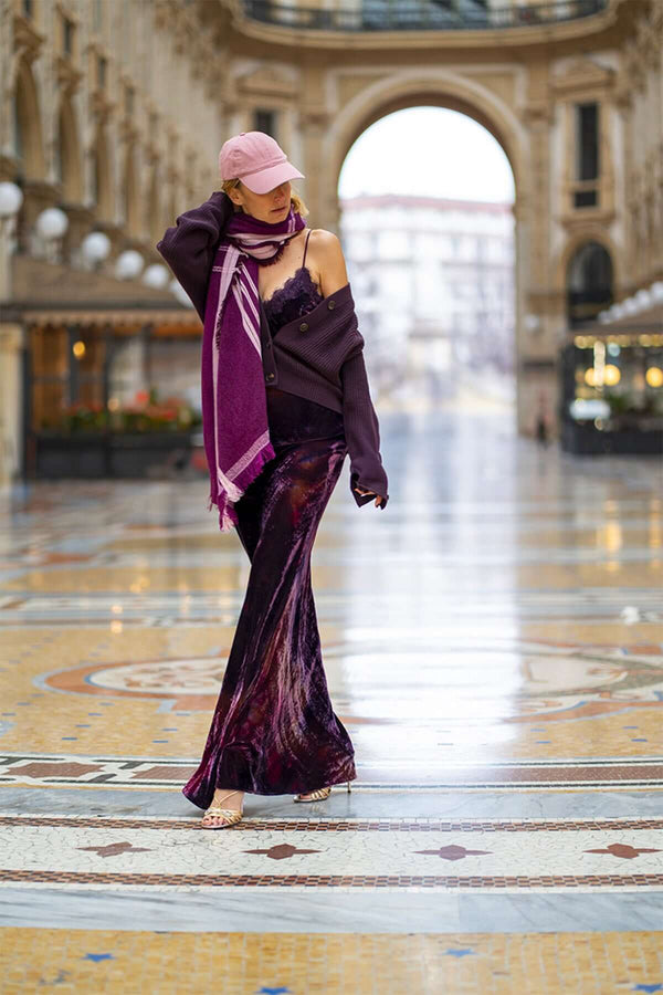 Model showcasing an elegant purple dress with a matching scarf and cap in an architecturally stunning gallery.
