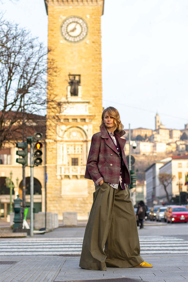 Fashionable woman in a stylish plaid jacket and wide-leg pants posing near a clock tower in a city street.