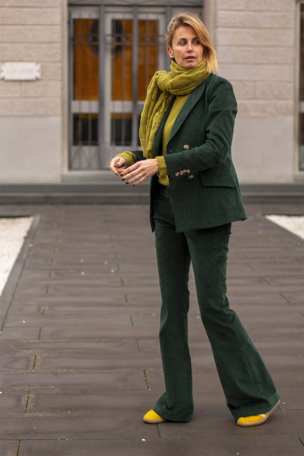 Woman wearing a green velvet suit with flared pants and a matching scarf, exuding elegance outdoors.